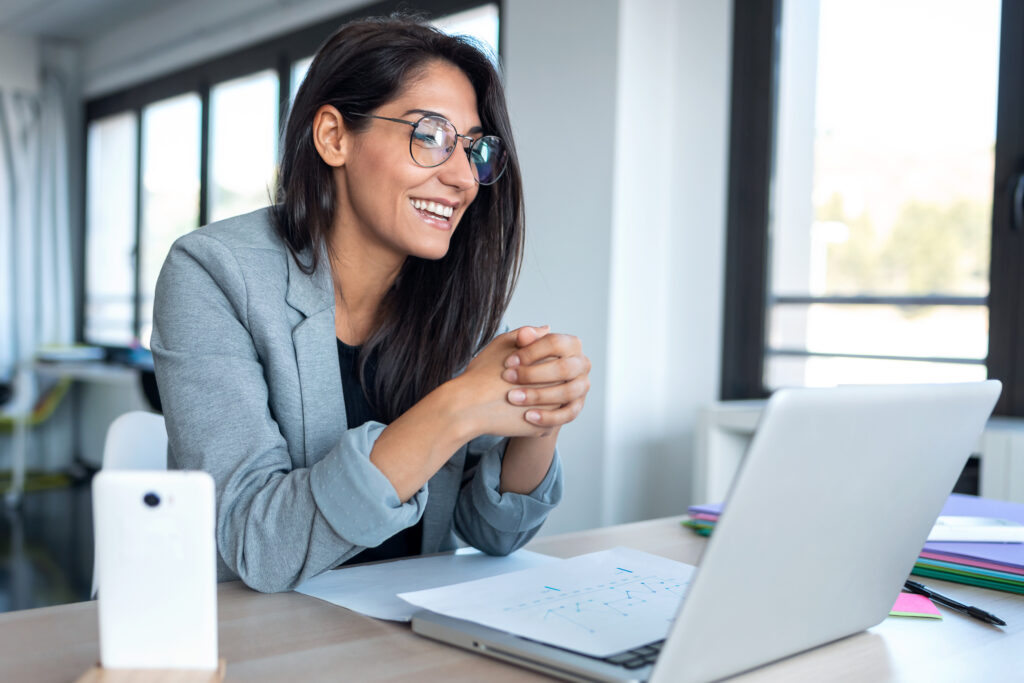 Shot of confident business woman looking and speaking through the webcam while making a video conference with laptop from the office.